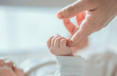 Image of a babies hand wrapped around an adults finger
