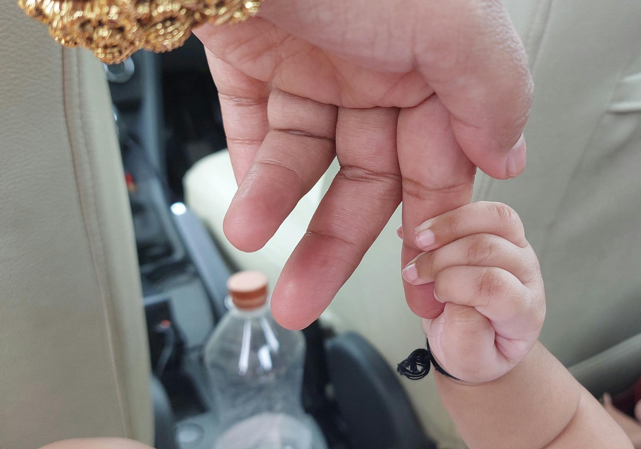 A baby holding an adult's finger in a car, showcasing a warm bond.