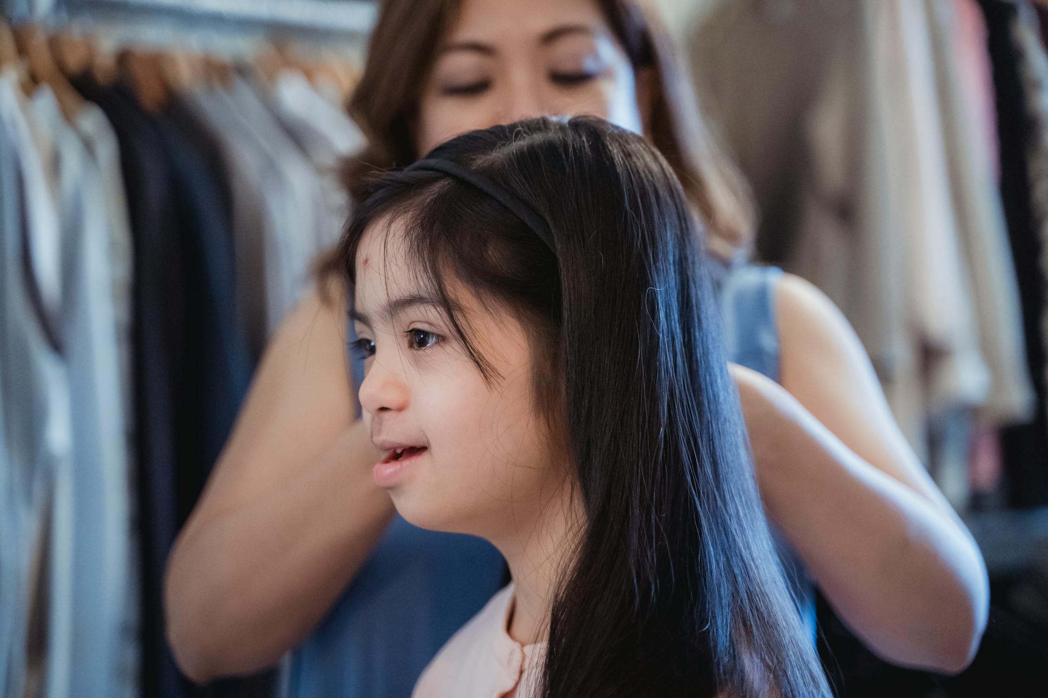 A mother lovingly helps her daughter fix her hair in a cozy indoor setting, showcasing family bonding.