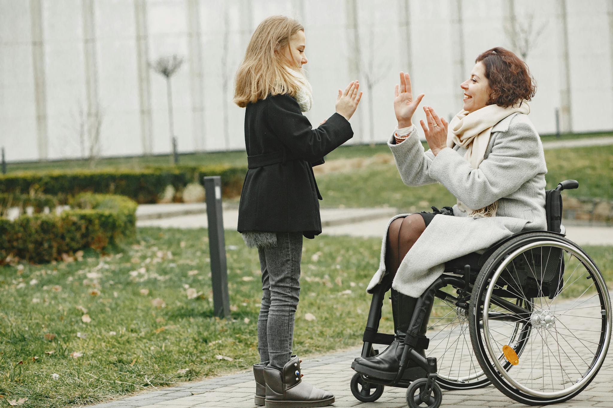 Happy child and woman in wheelchair sharing a joyful moment outdoors.